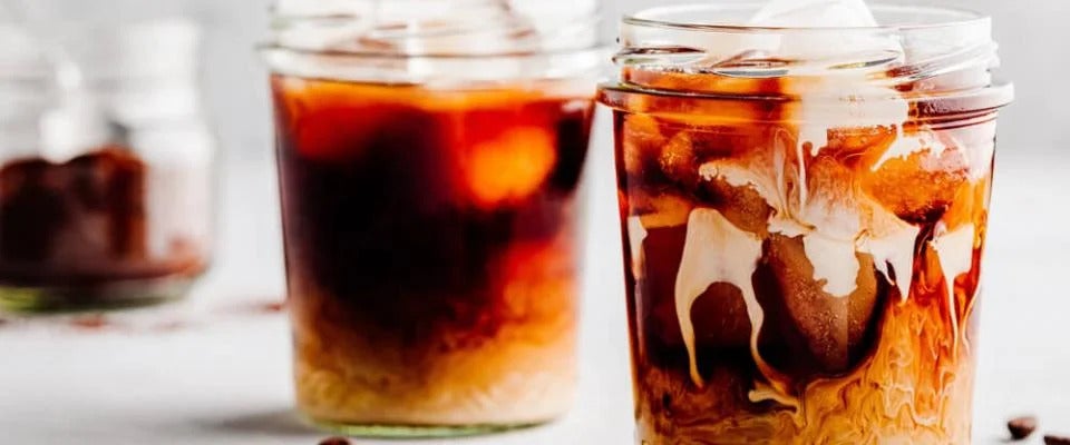 Two glasses of cold brew coffee with coffee beans scattered around them