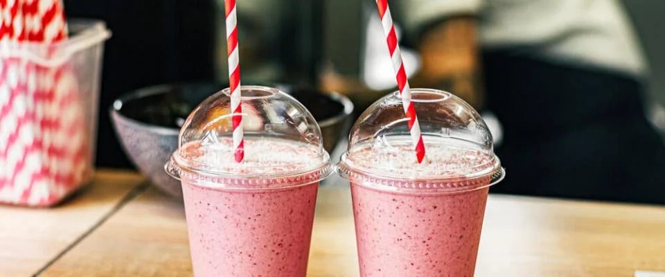 Two fruit smoothies on table with red and white straws
