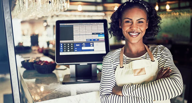 Waitress in apron smiling in front of point of sale terminal