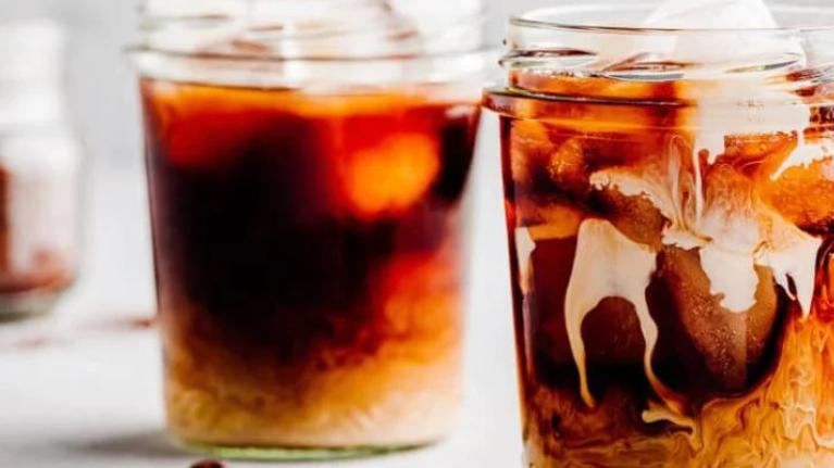 Two glasses of cold brew coffee with coffee beans scattered around them