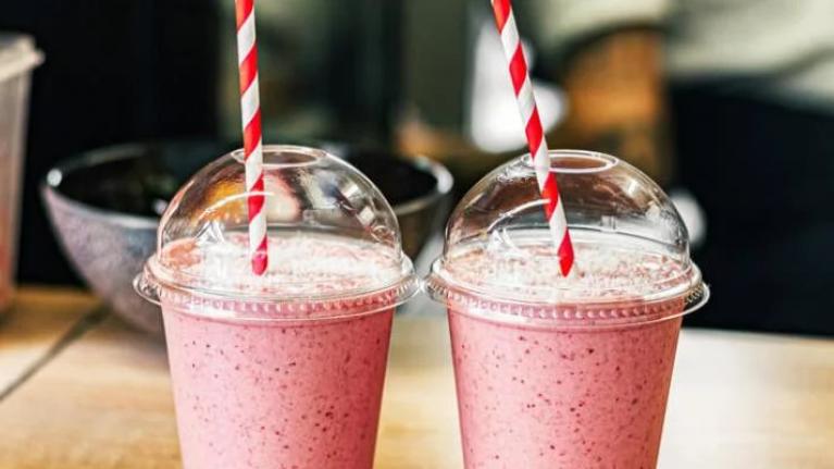 Two fruit smoothies on table with red and white straws