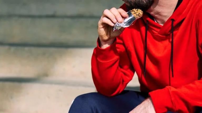 Tired sportsman sitting on stairs outdoors and eating energy bar
