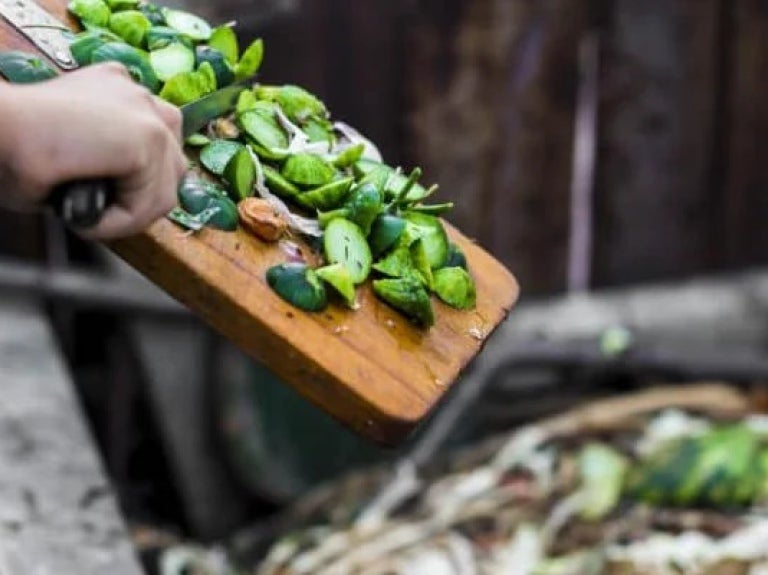 Green food scraps being scraped off cutting board into compost bin